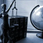 Statua Temidy z wagą i łańcuszkami obok globusa oraz ksiąg prawa, w tle poradnik adwokata