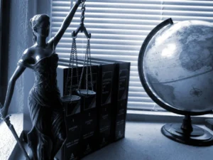 Statua Temidy z wagą i łańcuszkami obok globusa oraz ksiąg prawa, w tle poradnik adwokata