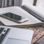 Smartfon i laptop na biurku obok notatnika, przygotowanie do założenia firmy w Norwegii